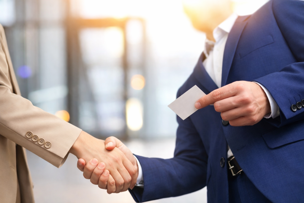 Two professionals shaking hands while exchanging a business card during a professional networking meeting